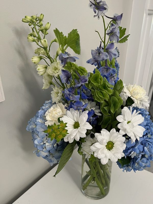 Blue hydrangea, delphinium and white daisies in a glass vase