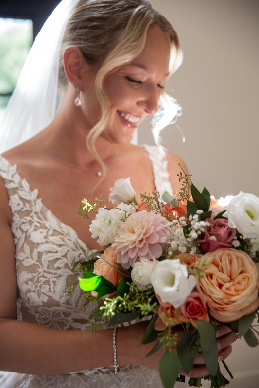 Bride looking down at her peach and white bouquet