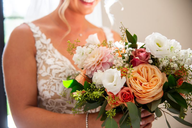 Bride holding a peach, white and coral bouquet