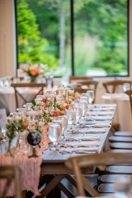 Farm table set with peach runner and floral arrangements by a window