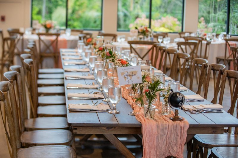 Reception hall with long farm tables, peach runners and bud-vase arrangements