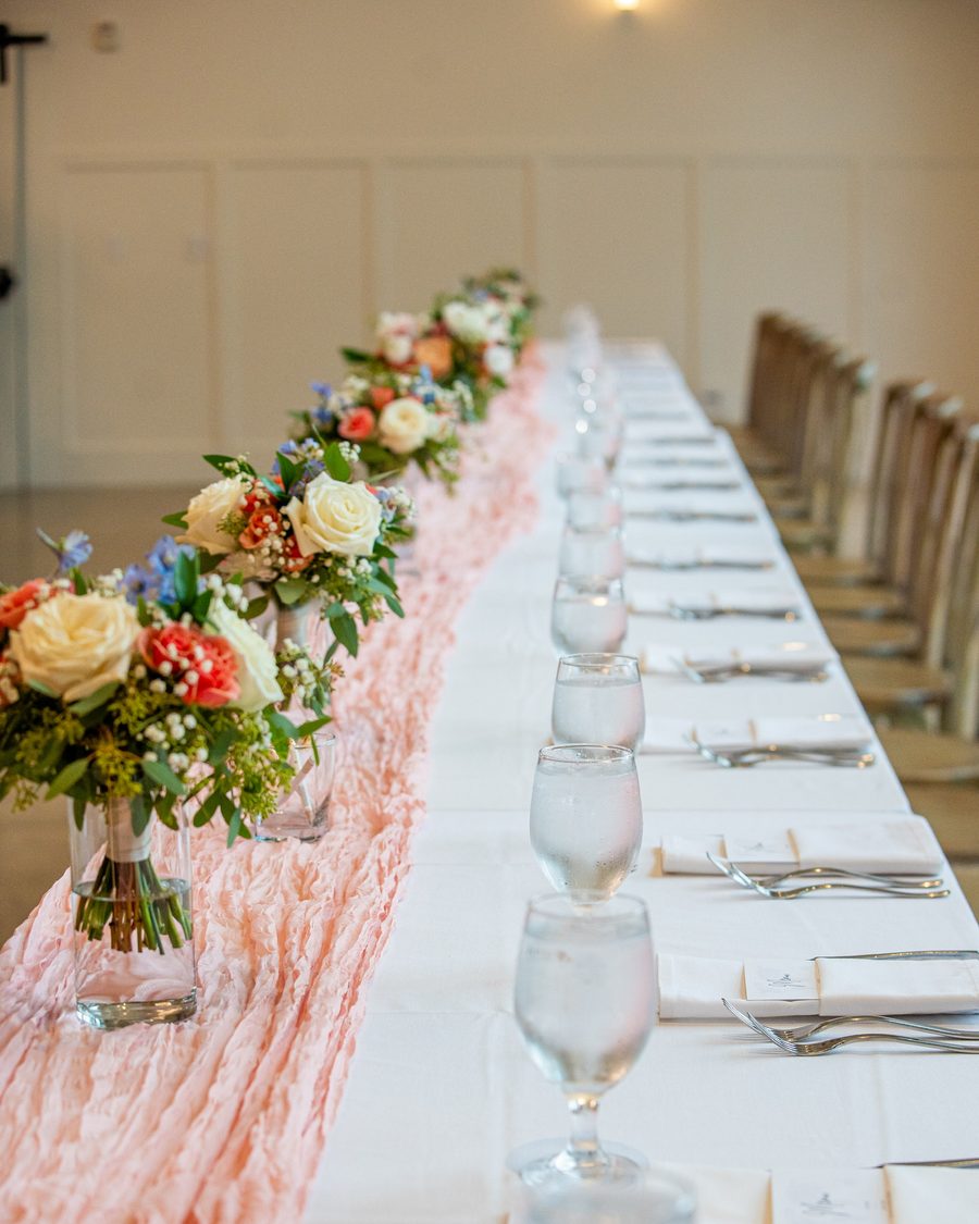 Long reception table with peach runner and floral arrangements