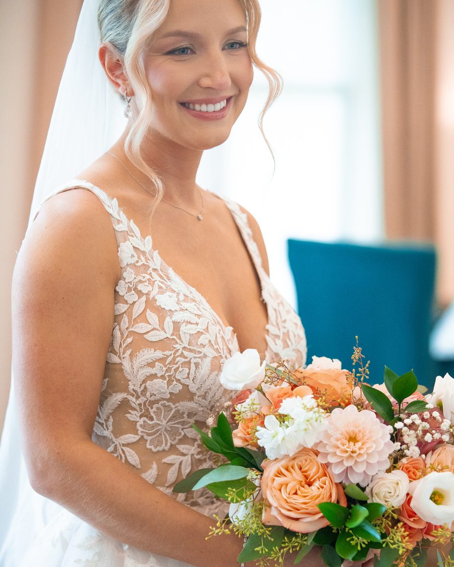 Smiling bride holding a peach and white bouquet
